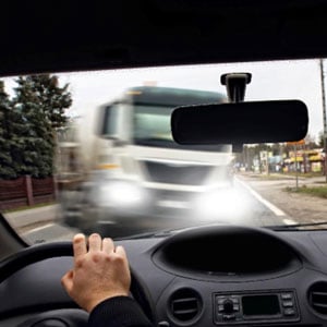 A hand grips the steering wheel, facing an oncoming truck on the road.